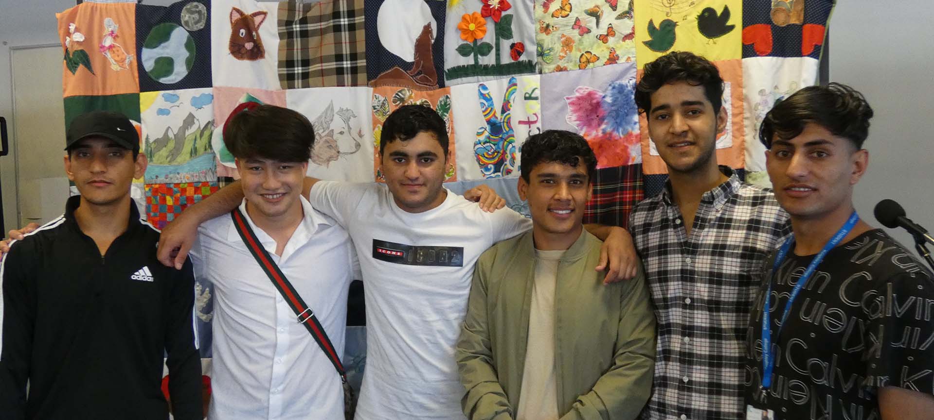 Three students smiling standing in front of creative patchwork quilt